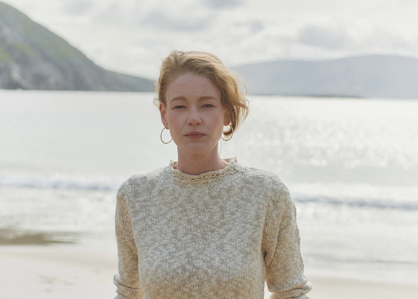 Dame im hellen Aran-Strickpullover vor weiter Küstenlandschaft
